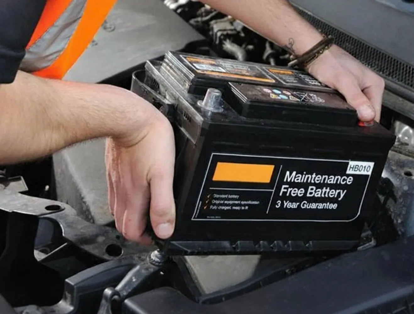 Hands lifting a maintenance-free battery out of a car