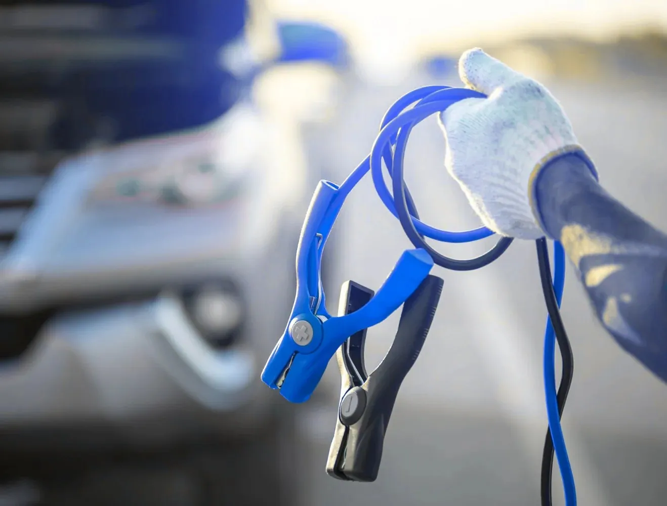Gloved hand holding blue jump leads